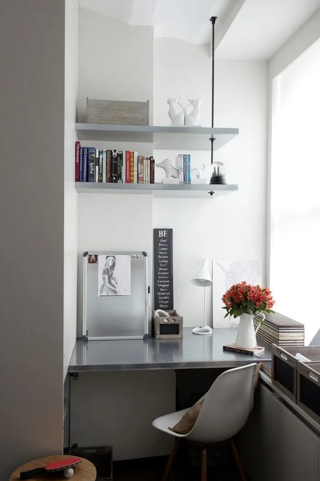 a contemporary home office created in a tiny awkward nook by the window, with a metal desk, a white chair, some shelves and crates for storage