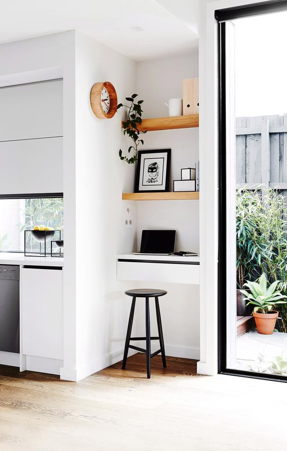 a super tiny working nook with built-in shelves and a small desk with drawers, a black stool, artworks and a potted plant