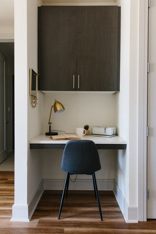 a tiny home office built into a small nook, with a built-in desk and a large cabinet, a navy chair, a brass table lamp