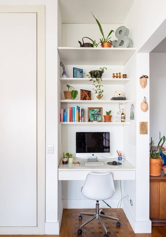 a tiny nook with built-in shelves and a desk with a drawer, a white chair, books and potted plants is a cool space fo working