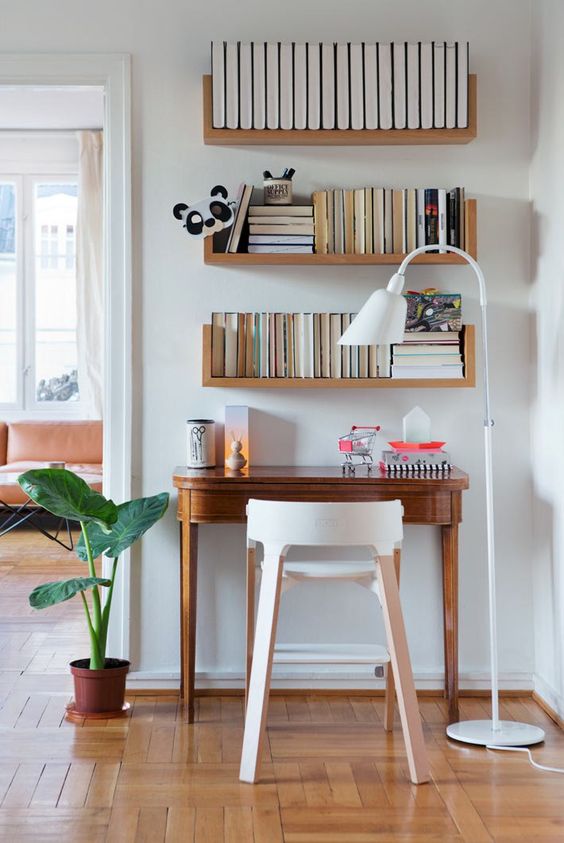 a small and stylish nook made a home office with three bookshelves and a vintage desk, a plywood stool and a cool floor lamp