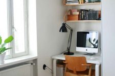 37 a small nook by the window with a white desk and some suspended shelves, a plywood chair and a black table lamp