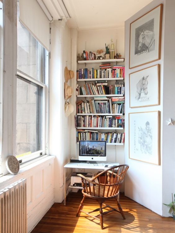 a tiny nook by the window with lots of shelves, a desk and a wooden chair, a gallery wall and some lights