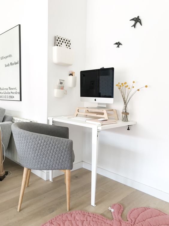 a working nook with a two-leg desk, a grey chair, a PC on a stand for more comfort and a series of box-like shelves