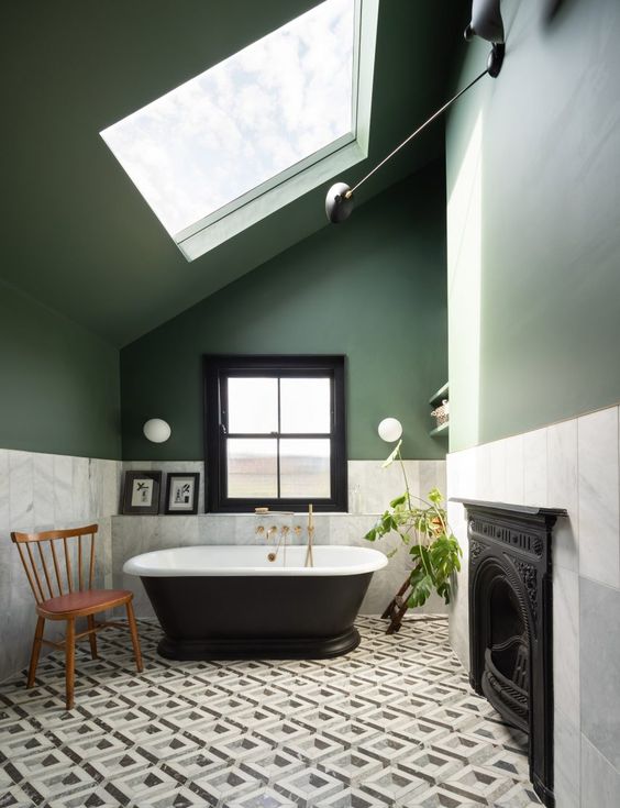 a beautiful bathroom with green walls, white marble tiles, a geo floor, a chic black bathtub and brass touches