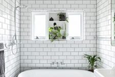 a beautiful black and white bathroom with white subway and black hex tiles, a free-standing sink, a black vintage bathtub and a window