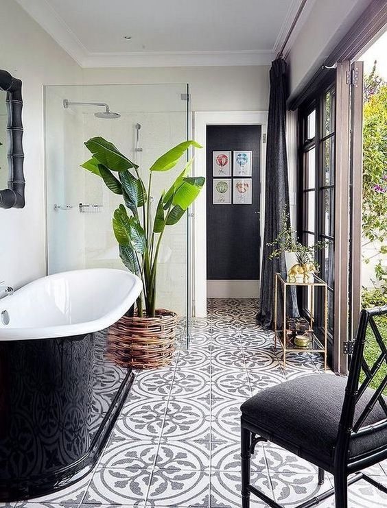 a beautiful indoor-outdoor bathroom with a printed tile floor, a glossy black tub, a shower, a statement plant in a basket and a black chair