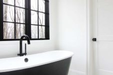 a black and white farmhouse bathroom with a black window frame, a sleek black bathtub, a cool chevron floor and a bubble lamp