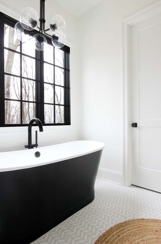 a black and white farmhouse bathroom with a black window frame, a sleek black bathtub, a cool chevron floor and a bubble lamp