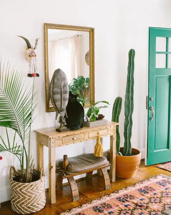 a boho summer console with a mask, greenery and a cactus around it and a cat on it