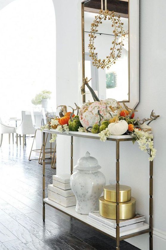 a chic console table with fake plastic and fabric pumpkins, white white blooms and a dried herb wreath over the table