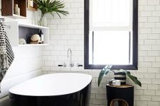 a chic modern bathroom with black patterned and white subway tiles, a sleek black bathtub and box shelves plus a black stool