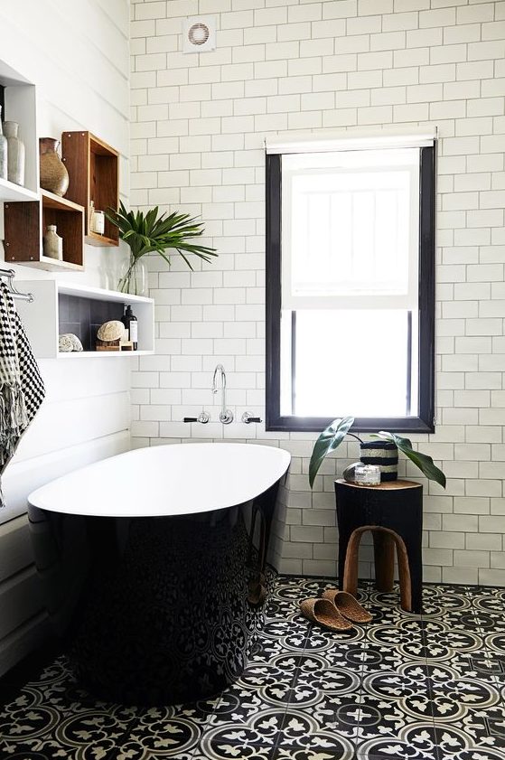 a chic modern bathroom with black patterned and white subway tiles, a sleek black bathtub and box shelves plus a black stool