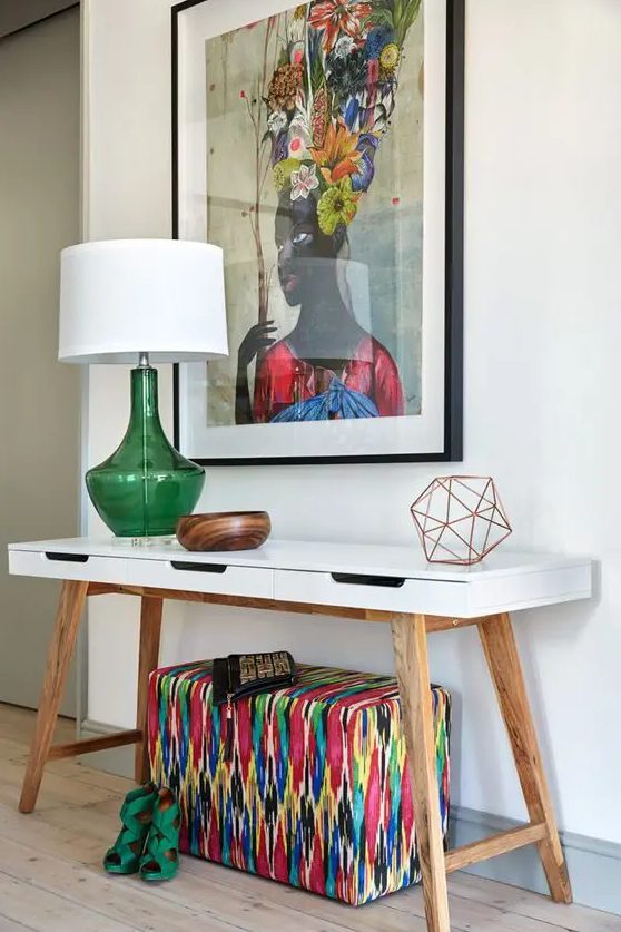 a chic white mid-century modern console table with a super colorful artwork, a bright upholstered ottoman and a green lamp for summer