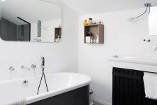 a contemporary black and white bathroom with white walls and laminate on the floor, a tub clad with black panels, a black paneled floating vanity and a rounded mirror