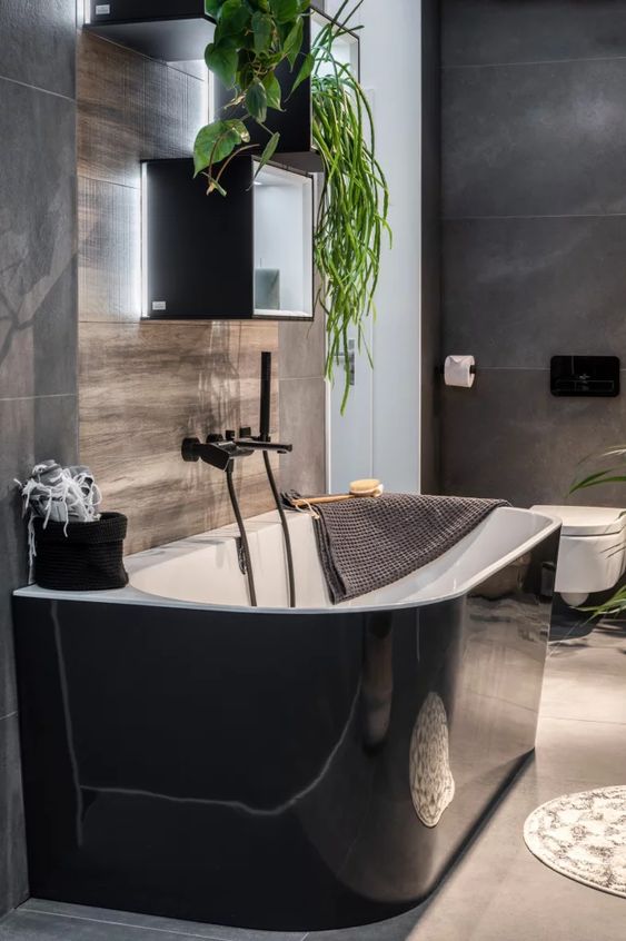 a contemporary moody bathroom with grey and wood tiles, with a glossy black bathtub and black box shelves is cool and edgy
