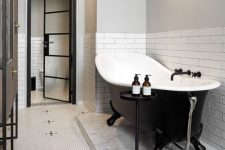 a cool modern bathroom with white subway tiles and penny ones, a black clawfoot tub, a brown vanty and a side table is all chic