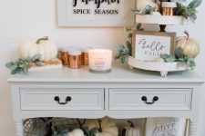 a cozy neutral Thanksgiving console table with lots of natural and faux pumpkins, greenery, candles and signs