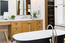 a farmhouse bathroom with a light-stained vanity, a couple of mirrors, a matte black bathtub and pendant lamps