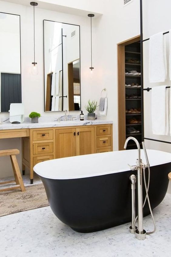 a farmhouse bathroom with a light-stained vanity, a couple of mirrors, a matte black bathtub and pendant lamps