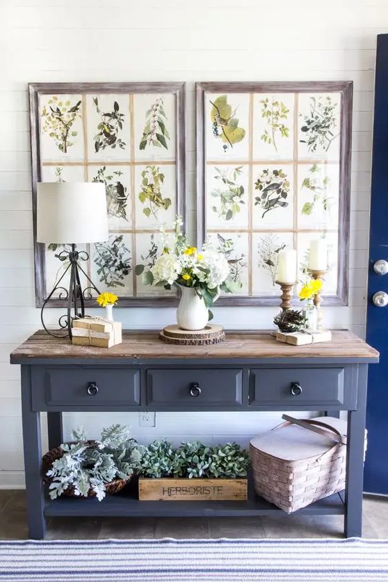 a farmhouse console table with a wooden countertop, much greenery in baskets and boxes, vintage botanical posters