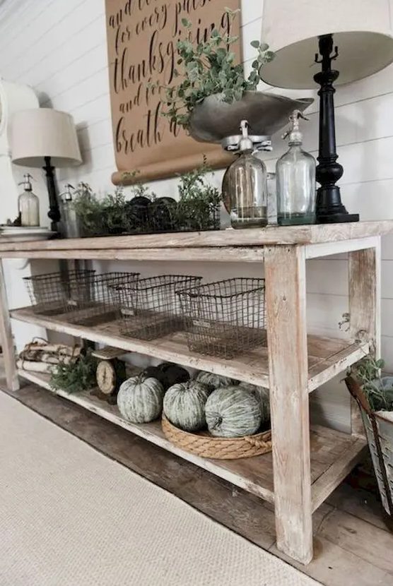 a farmhouse whitewashed console with green whitewashed pumpkins, greenery, wire baskets and lamps