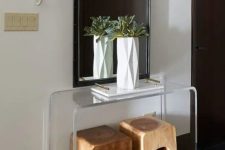 a minimalist acrylic console table, wooden stools, a geometric vase with greenery and a large mirror as a statement piece