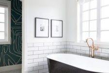 a modern bathroom with two different types of tiles, a sleek black clad tub, a catchy pendant lamp and printed wallpaper