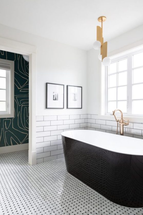 a modern bathroom with two different types of tiles, a sleek black clad tub, a catchy pendant lamp and printed wallpaper