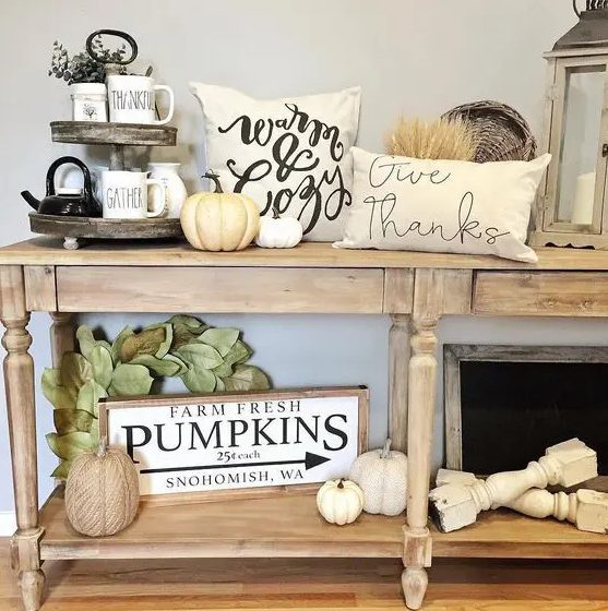 a neutral fall console table with white natural and faux pumpkins, wheat, leaves and printed pillows