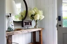 a rough wood console table, a round mirror in a black frame, white hydrangeas, a catchy lamp and a carved wood artwork for a cozy rustic look