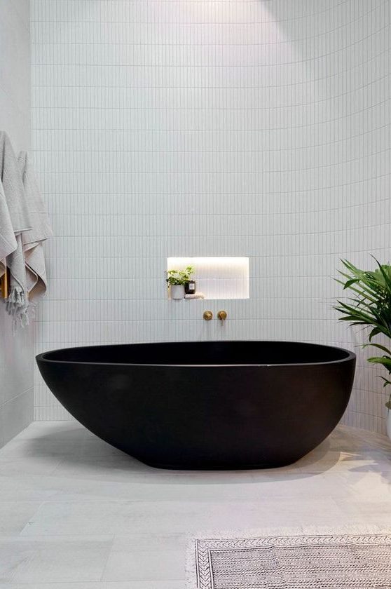 a sleek contemporary bathroom with large scale and skinny white tiles, a black stone bathtub and some neutral textiles