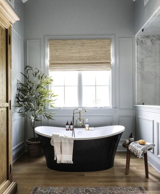 a sophisticated neutral bathroom with grey panels on the walls, a sleek black tub, shades, a printed rug and alight-stained wardrobe