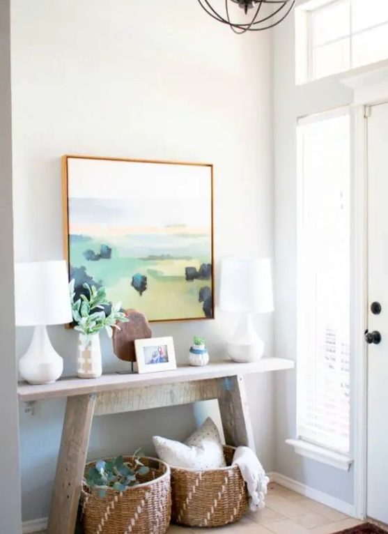 a summer console with an abstract artwork, baskets, elegant white table lamps and greenery for a cozy feel