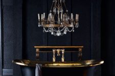 a super elegant bathroom with a luxurious feel, wallpaper walls, a black herringbone floor, a black and gold bathtub and a crystal chandelier