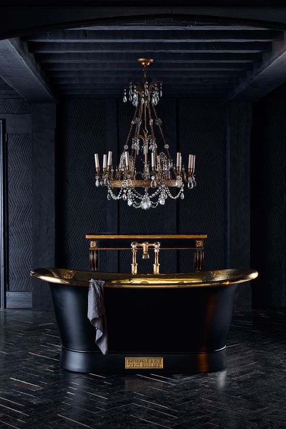 a super elegant bathroom with a luxurious feel, wallpaper walls, a black herringbone floor, a black and gold bathtub and a crystal chandelier