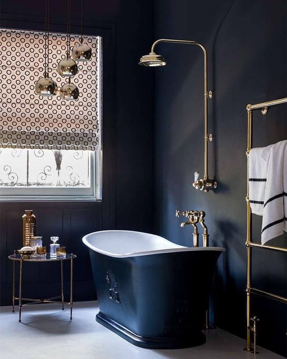 a vintage black bathroom with black walls, a vintage black bathtub, chic brass fixtures and a printed curtain on the window