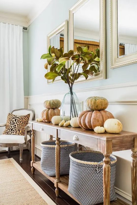 a vintage farmhouse console table with chevron baskets, natural pumpkins stacked on each other and fall leaves in a vase