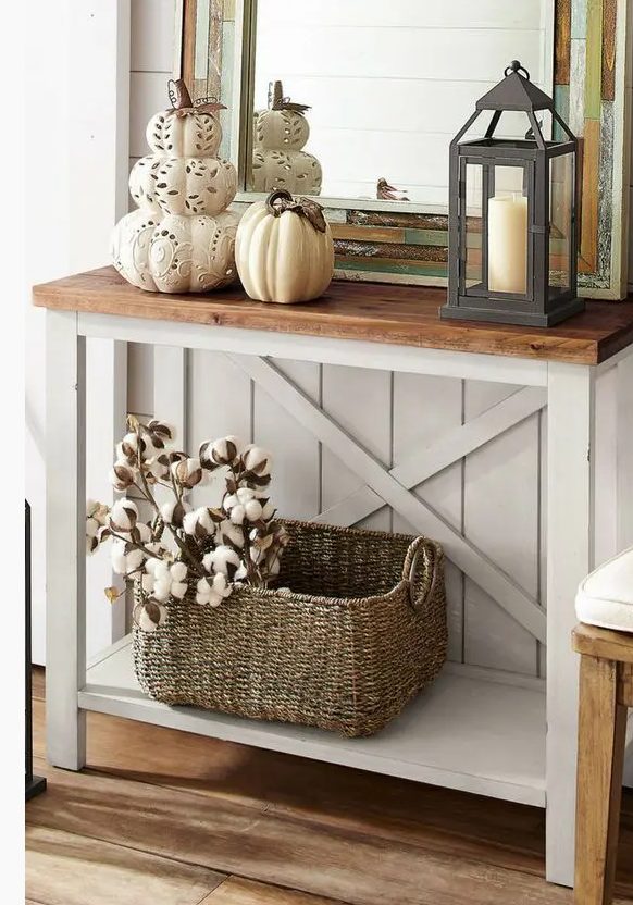a vintage rustic console with laser cut pumpkins and a porcelain one, a candle lantern and a basket with cotton branches