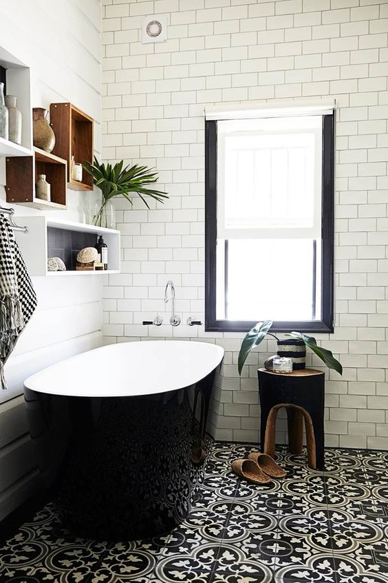 an elegant monochromatic bathroom with white subway tiles, a printed black and white floor, a glossy black bathtub, box shelves and a black stool