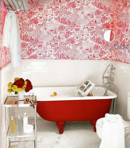 a small bright bathroom with red and white printed wallpaper, white subway tiles, a small red bathtub, an elegant tiered table and white appliances