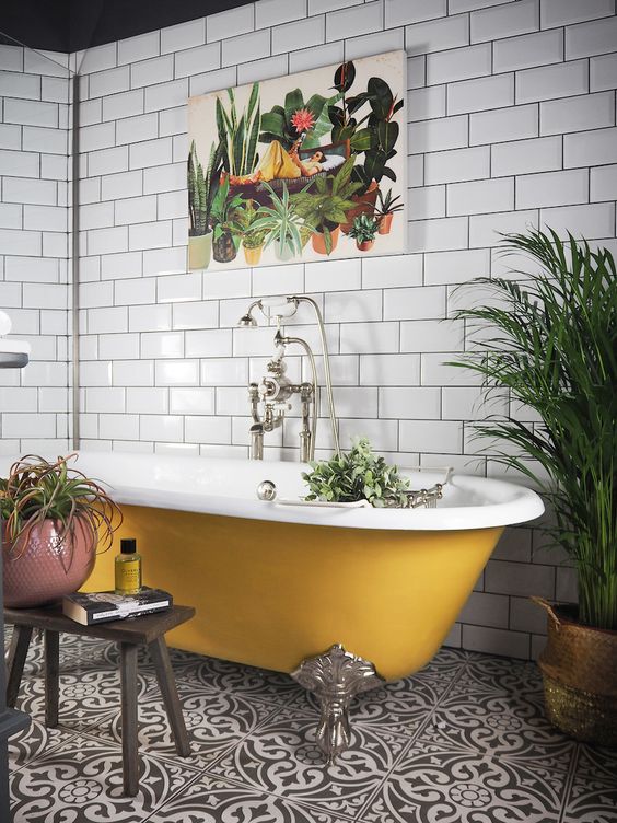 a black and white tile floor, white subway tiles on the walls, a mustard clawfoot bathtub and potted plants plus a bold print