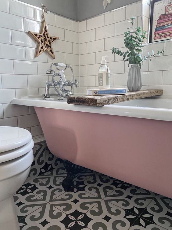 a small and pretty bathroom with a printed tile floor, a pink clawfoot bathtub, white subway tiles, greenery and white appliances