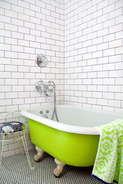 a simple bathroom with white subway tiles and penny ones on the floor, a neon green clawfoot bathtub and a matching bold towel