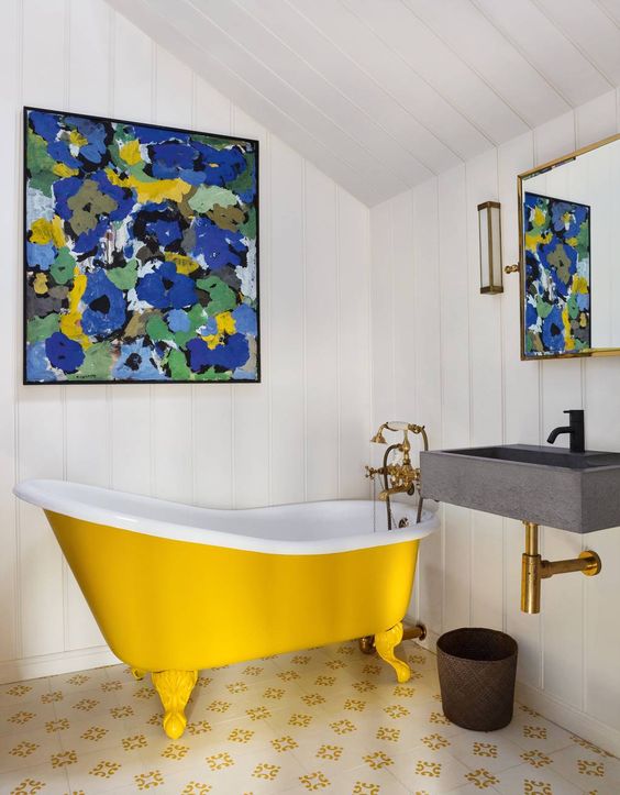 a small attic bathroom with white shiplap, a yellow clawfoot bathtub, a wall-mounted sink, a bright artwork and a mirror