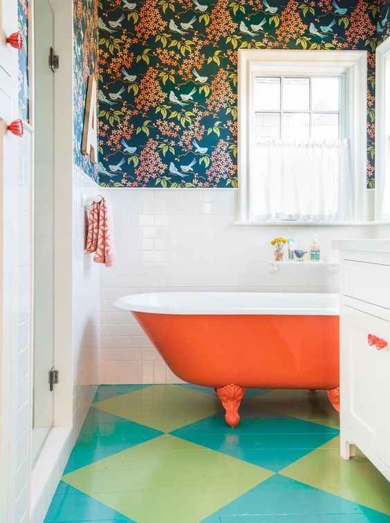 a colorful bathroom with dark floral wallpaper, white subway tiles, an orange bathtub, a bright green and turquoise floor and white textiles