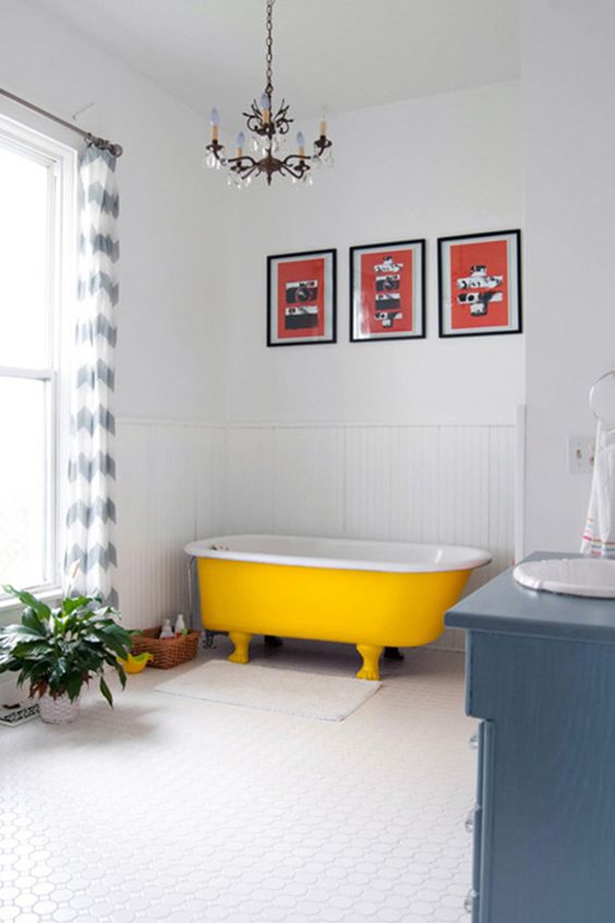 a crispy white bathroom with a bold yellow clawfoot bathtub, a blue vanity, a colorful gallery wall and a potted plant
