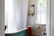 20 a farmhouse bathroom with white shiplap on the wall, a green clawfoot bathtub, a wooden floor, a vintage chair and neutral textiles