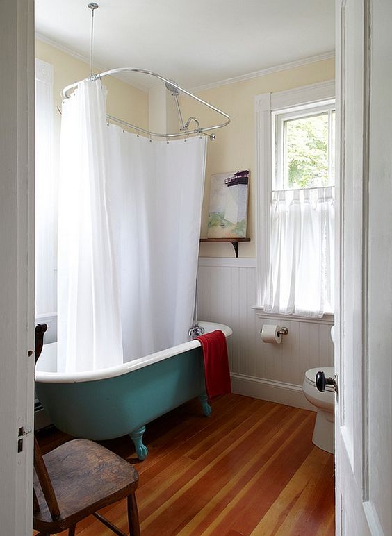 a farmhouse bathroom with white shiplap on the wall, a green clawfoot bathtub, a wooden floor, a vintage chair and neutral textiles