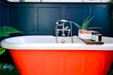21 a moody bathroom with black paneling, a contrasting tile floor, an orange bathtub, potted plants and some art and books